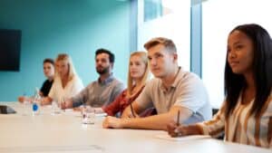 Group of Young Employees Sitting At Boardroom Table Listening To Training Seminar.